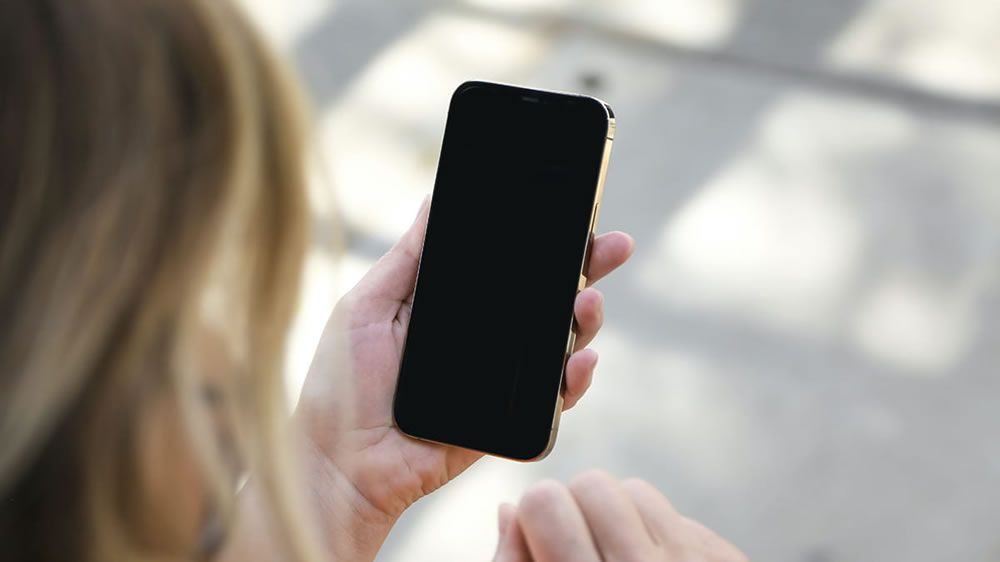 Smartphone à l'écran noir tenu à la main en extérieur, l'appareil ne réagit plus